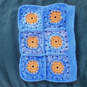 A crocheted granny square clutch bag featuring patterns inspired by Van Gogh's paintings. It has a zip closure.