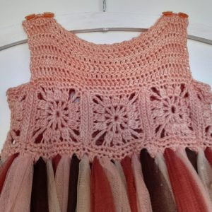 Close-up of a hand-crocheted salmon-colored cotton bodice for a toddler dress, featuring playful granny squares around the waist.