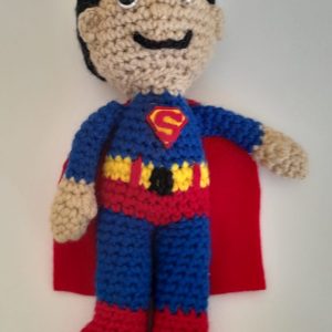 Superman Soft Toy. Toy of Superman crocheted from yarn, displayed wearing a detailed blue suit with red cape and yellow "S" insignia, handcrafted by South African artisan Pippie Langbeen.