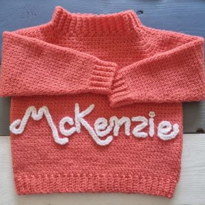 Photo of a pink crochet baby jersey with the a name chrochet to embellish the jersey.
