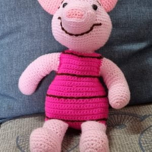A 35cm tall Piglet Crocheted Soft Toy from Winnie the Pooh sitting with he couch.
