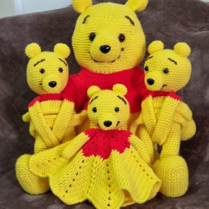 Photo showing a 40cm crocheted Winnie the Pooh soft toy sitting alongside a 20cm crocheted Pooh lovey plush and 2 Pooh curtain tiebacks.