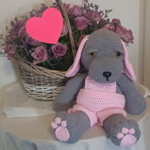 Front view of a 40cm grey and red crocheted doggy soft toy sitting on the couch.