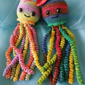 Crochet Octopus Cuddles. Multi-colored cotton crocheted octopus toy curled up on rocky ocean floor backdrop, approximately 30cm long, crafted by Pippie Langbeen in South Africa.