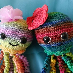 Multi-colored cotton crocheted octopus toy curled up on rocky ocean floor backdrop, approximately 30cm long, crafted by Pippie Langbeen in South Africa.